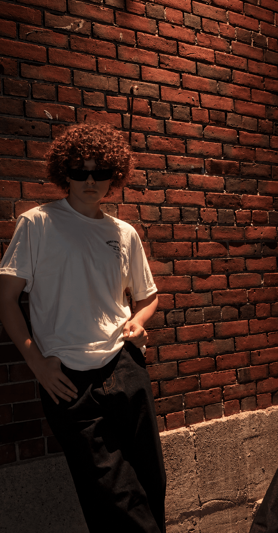 Celura tee styled with black pants against a brick wall