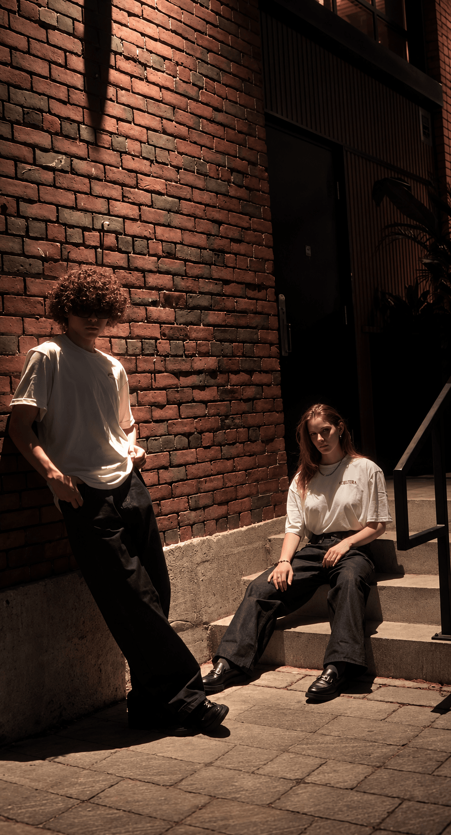 Two models wearing Celura tees beside a brick wall